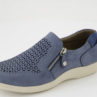 A blue slip-on shoe with a geometric laser-cut pattern on the toe, a silver zipper on the side, and a thick cream-colored sole, shown against a plain white background.