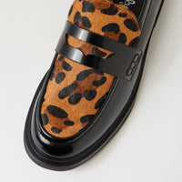 A close-up of a loafers shoe featuring a brown and black leopard print hair-on-hide upper with a glossy black leather strap and sole.